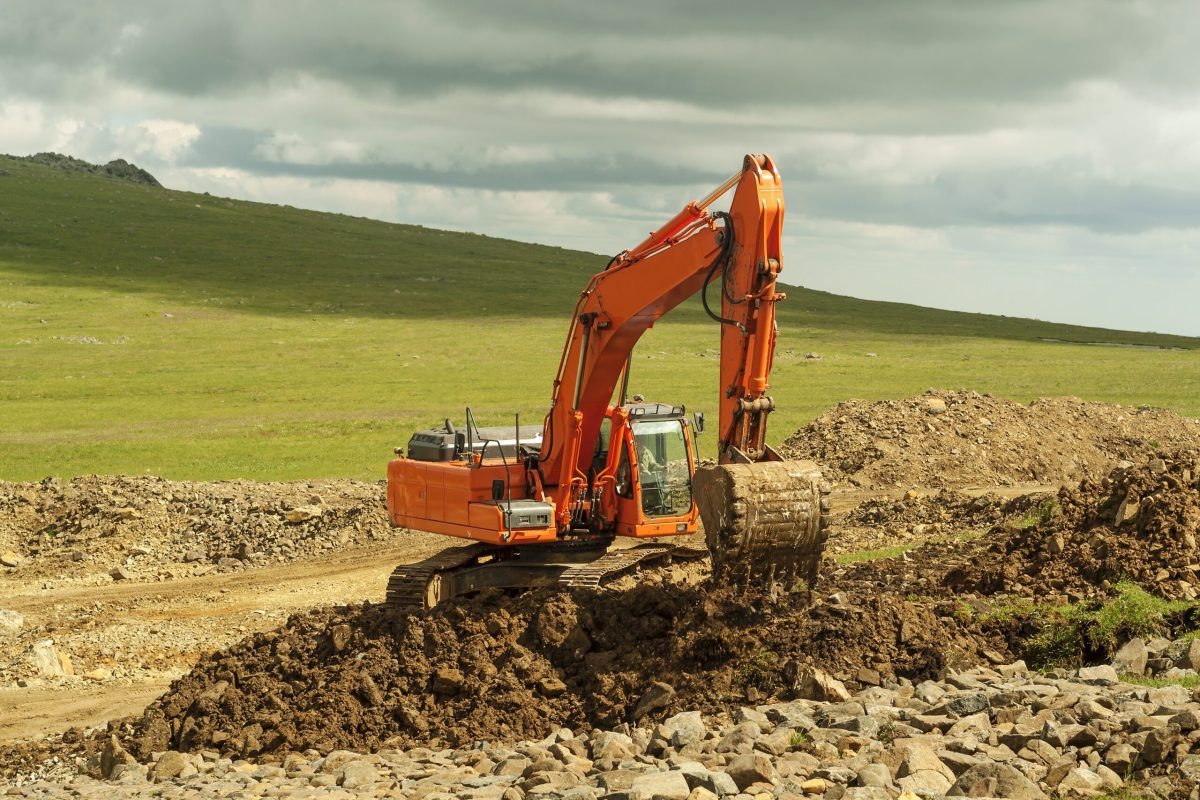 bright orange excavator working in a deserted mountain landscape